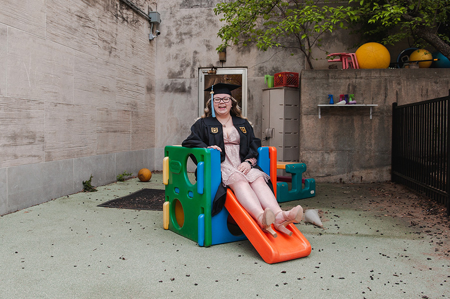 Rachel Sacharin posing for a graduation picture while sitting on a small slide.