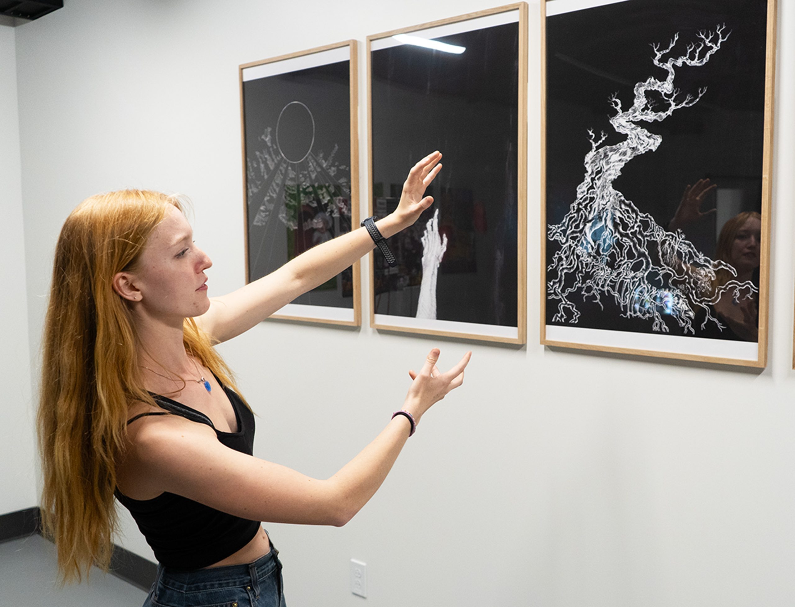 A student showcases their artwork that is hanging on the wall.