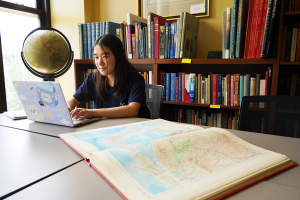 Faith Quist working on her laptop while a map lays on the table beside her.