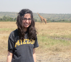 Kanwal Haq smiling for a picture with a giraffe in the background.