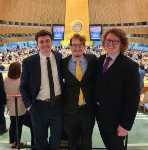 A group of three students, wearing suits, smiling at the camera for a photo.