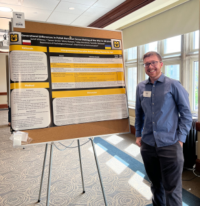 A student smiling at the camera while standing by their research presentation.