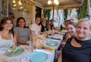 A group of individuals smile for the camera while sitting around a table before a meal.