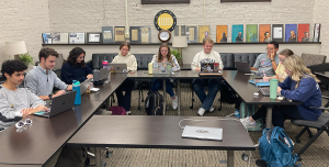 A group of students sitting around tables doing work.