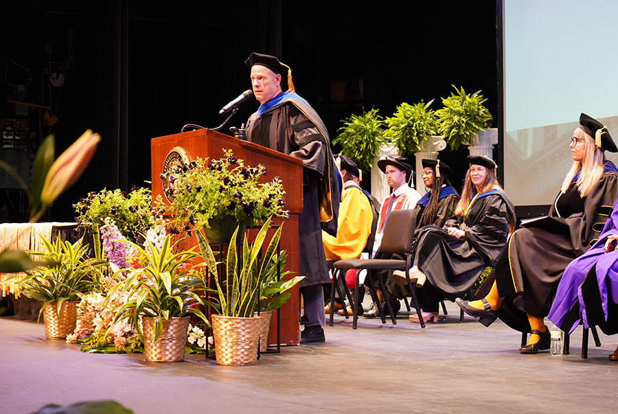 Troy Hall standing at a podium, speaking to a crowd during graduation.