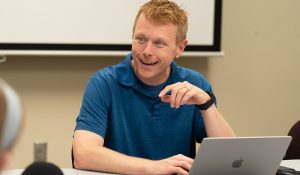 Chris Josey smiling while sitting in front of his laptop and talking to a student.