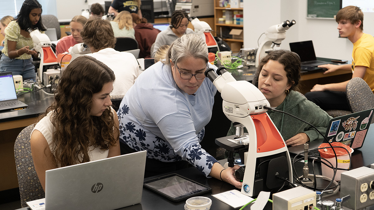 Pam Brown teaching students as they all look at a microscope.