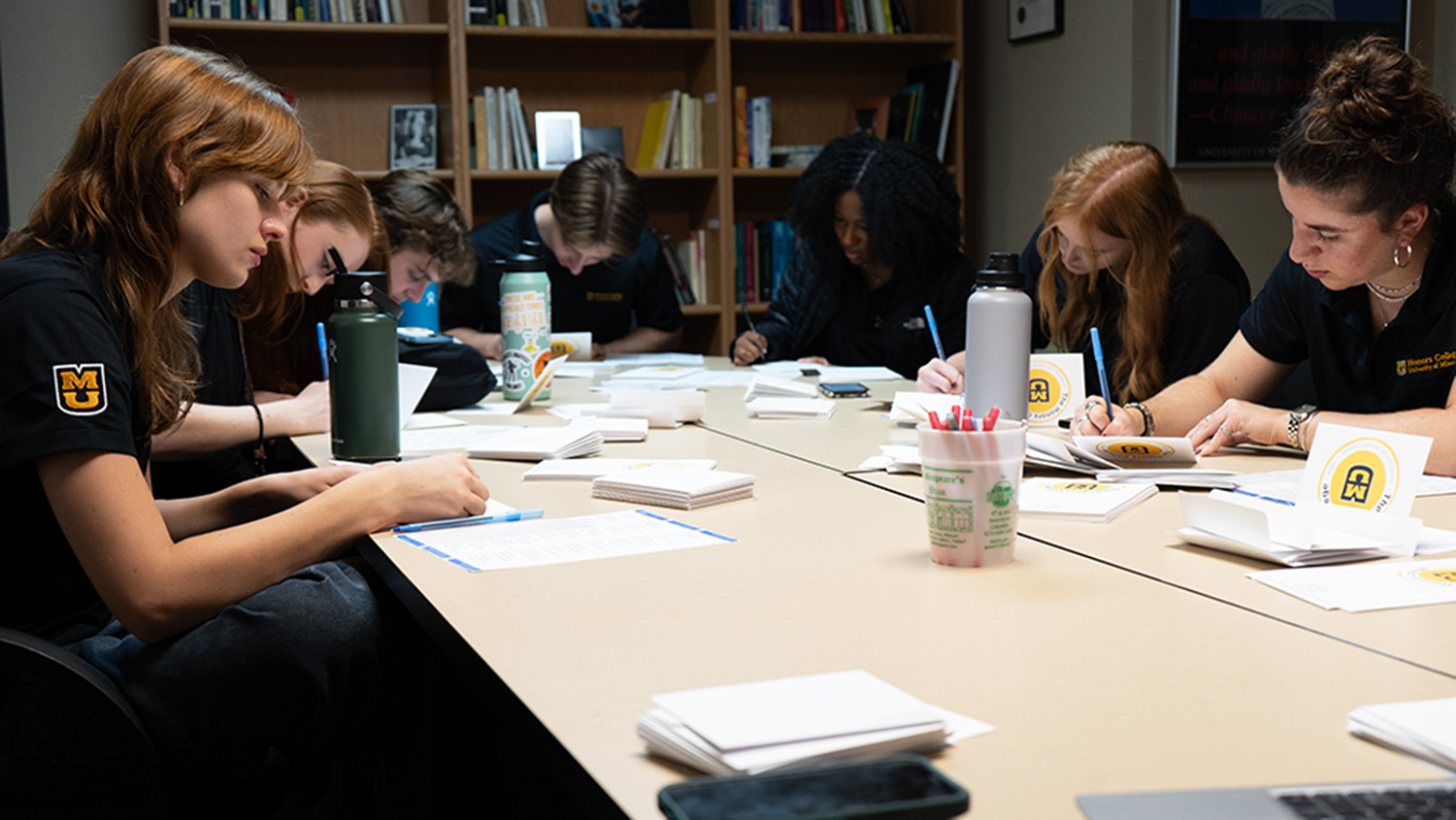 A group of students sitting around a table writing letters to accepted students.