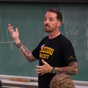 Doug Valentine standing in front of a chalkboard, teaching a class.