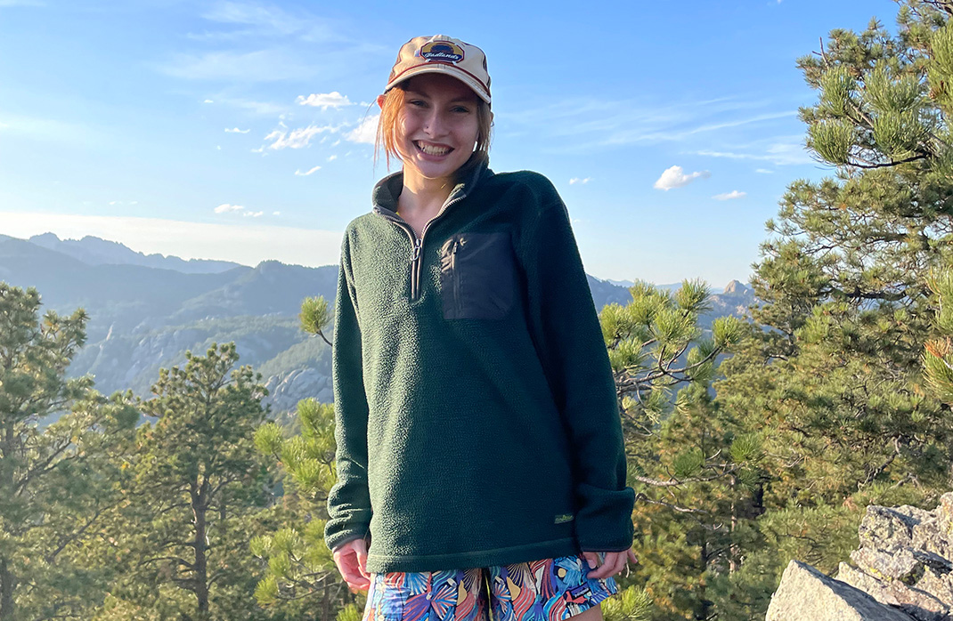 Emma Knudson posing for a picture in front of several trees.