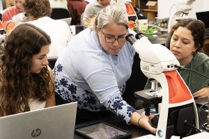 Pam Brown teaching students as they all look at a microscope.