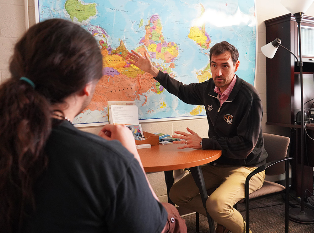 Erik Potter talking to a student about fellowship opportunities while pointing at a map.