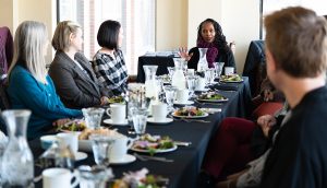 A group of faculty sitting around a table listening to an individual talk.