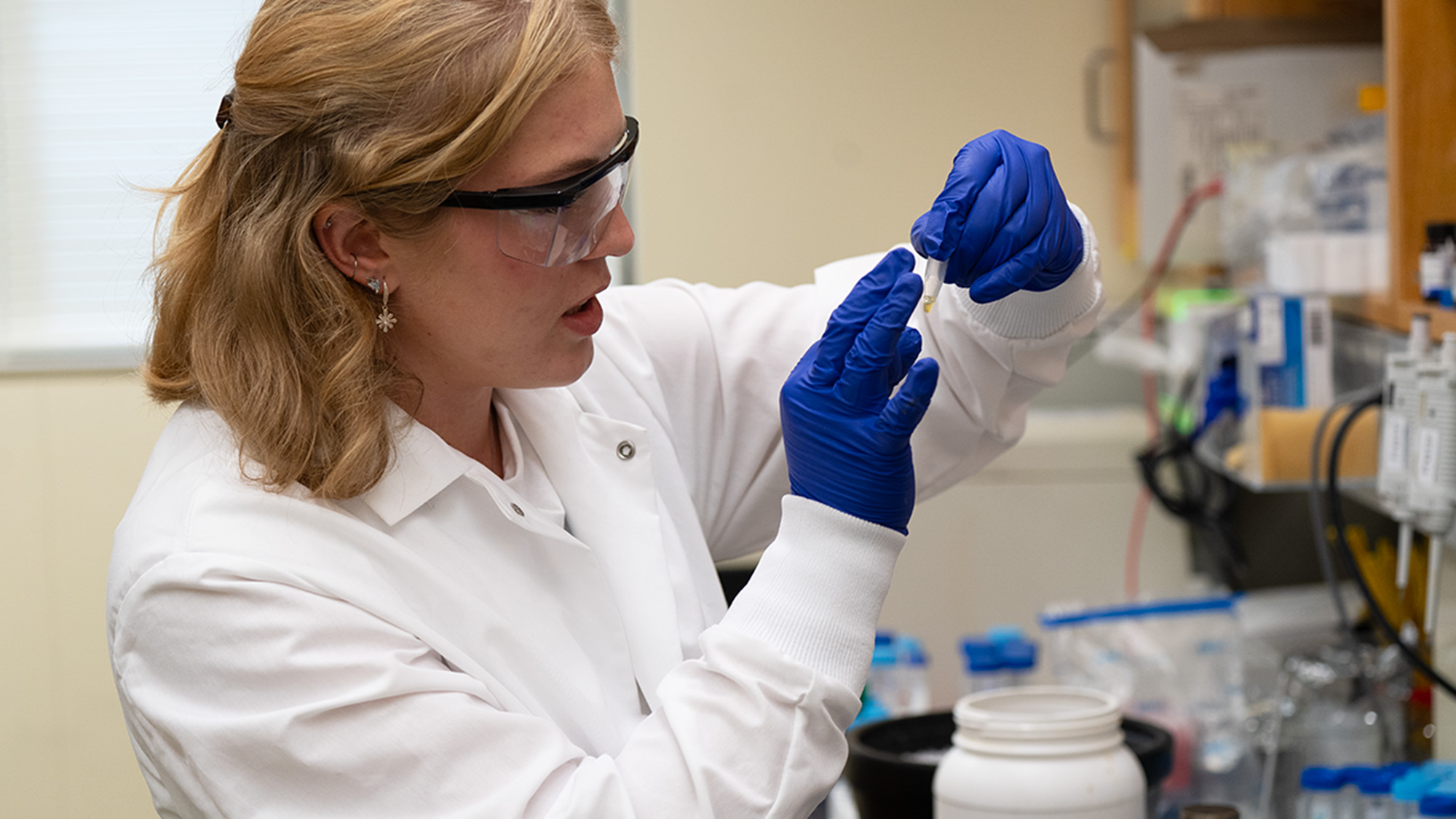 A student in a lab coat working with lab equipment.