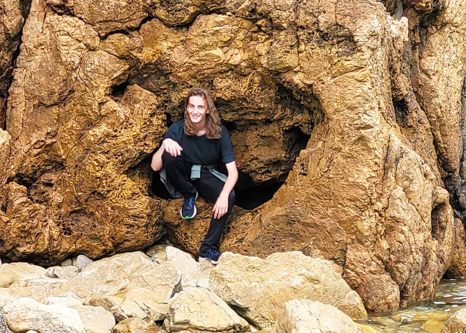 Jasper Holland posing for a picture while sitting by an entrance to a cave.