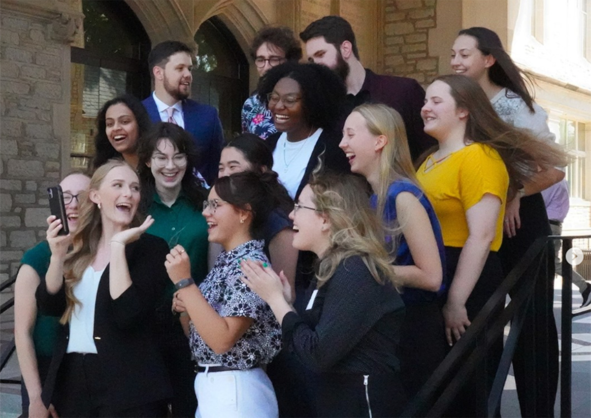 A group of more than 10 students laughing and smiling while taking a selfie.