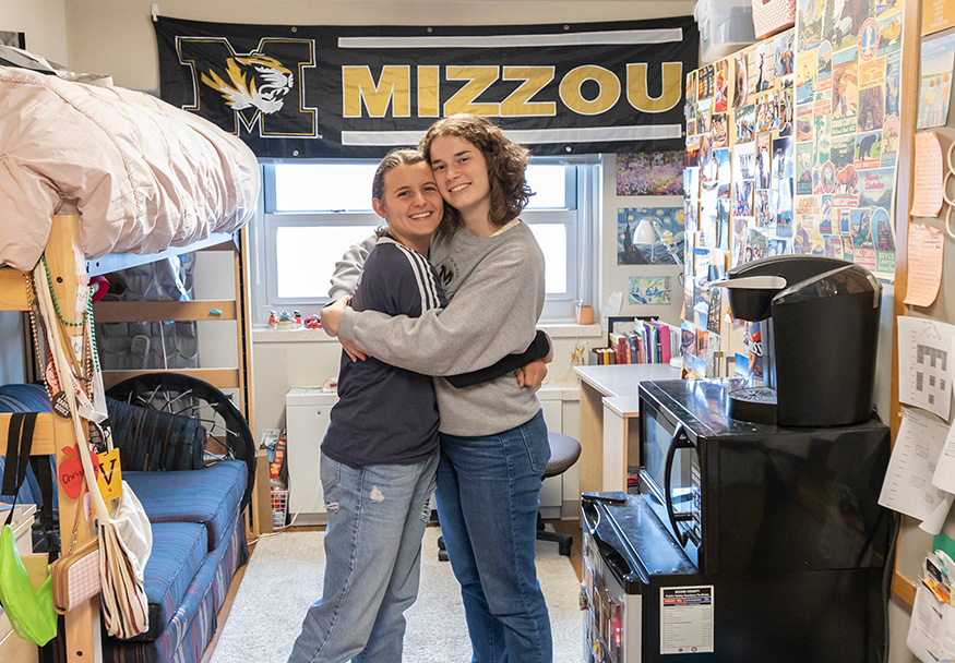 Two students hugging while standing in their dorm room.