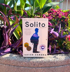 A picture of the book, Solito, in front of a bed of flowers.