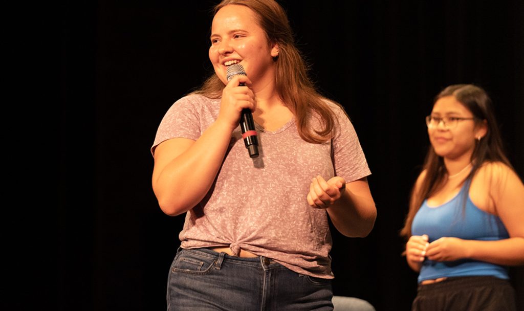 A student talking into a microphone to a group of students.