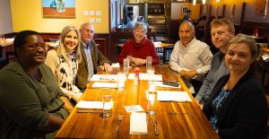 A group of individuals sitting around a table smiling for a group picture.