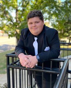 TJ Benoist posing for a picture outside while wearing a suit and tie.