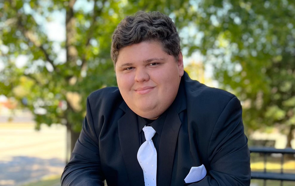 TJ Benoist posing for a picture outside while wearing a suit and tie.