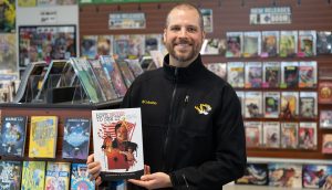 Andrew Fialka holding his graphic history book and smiling for a photo.