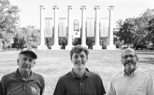 Three individuals smiling and posing for a photo in front of the Mizzou Columns.