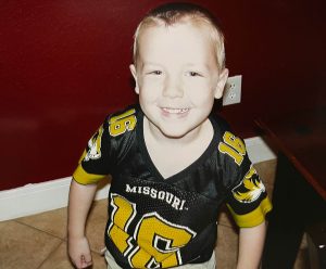 A picture of Sam Ennis, when he was a toddler, wearing a Mizzou football jersey and smiling for a photo.