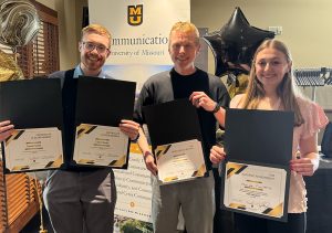 Three individuals smiling for a picture while holding awards.