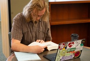 Graham George reading a book while sitting in the library.