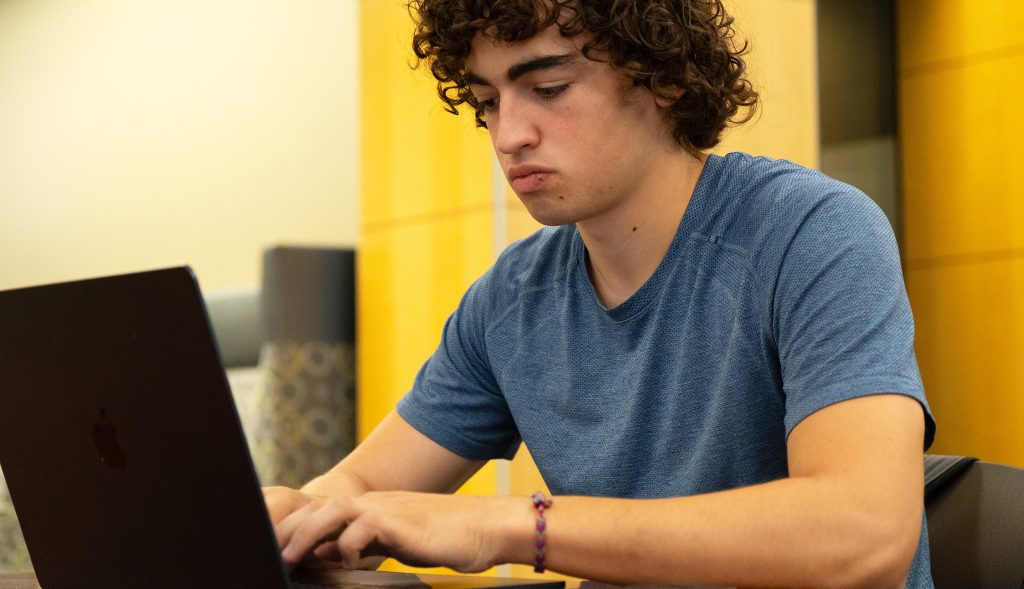 Josiah Anderson working on his laptop while sitting in the library.