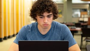 Josiah Anderson working on his laptop while sitting in the library.