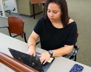 Nya Dodd working on her laptop while sitting in a library.