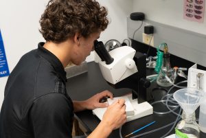 Zach Wright looking into a microscope while performing a research task in a laboratory.