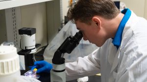 Cole Stevens looking into a microscope while in a research laboratory.