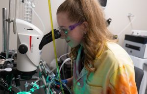 Ava Fleury sitting and looking into microscope in a research laboratory.
