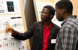 Joseph Oyewsui pointing at a research poster while talking to another individual about his research.