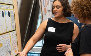 Alexandra Renoe pointing to her research poster while discussing her research with another person.