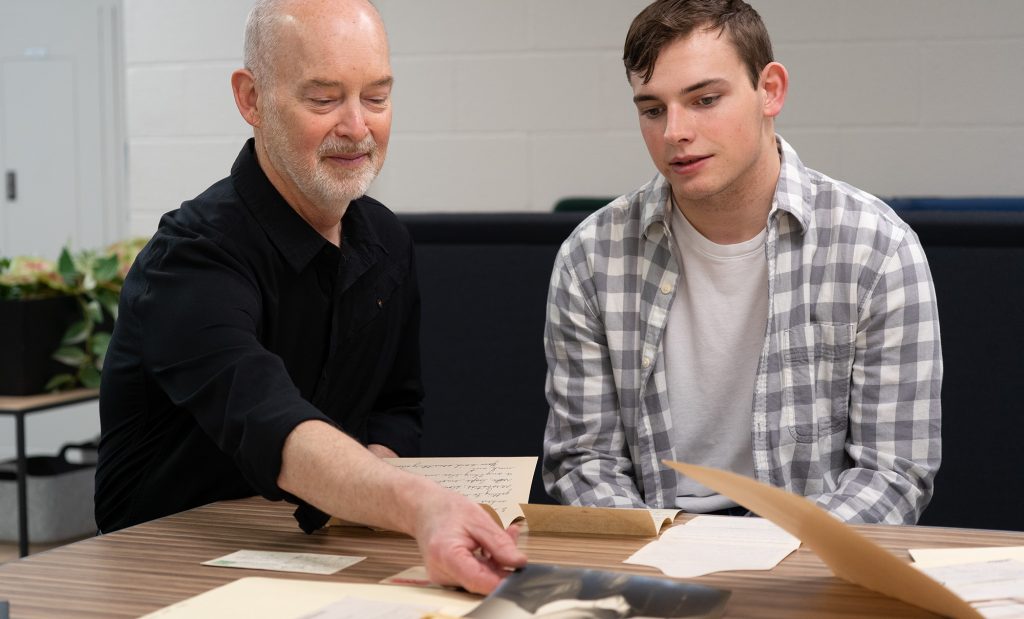 Two individuals sitting at a table and looking at various documents.