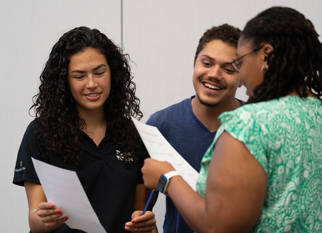 Three students smiling while talking to each other and completing an assignment.