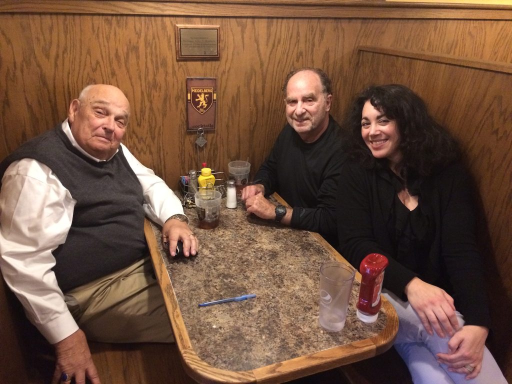 Three individuals, sitting in a restaurant booth, smile while posing for a picture.