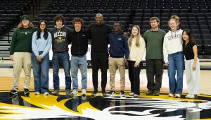 A group of students smiling while posing for a picture with Dennis Gates. They are all standing on the Mizzou basketball court.