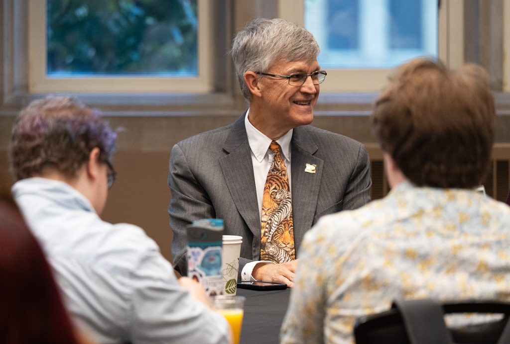 Jim Spain smiling while talking with other individuals.