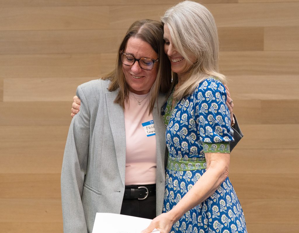 Two individuals smiling and hugging during an awards ceremony.