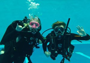 Two individuals scuba diving in complete scuba gear.