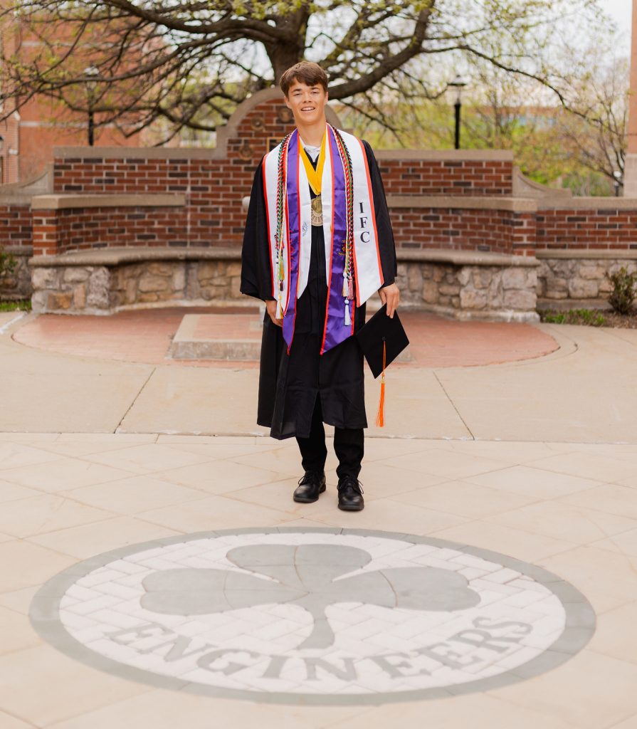 Wyatt Carlson dressed in graduation robes and smiling while posing for a photo.