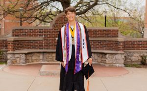 Wyatt Carlson dressed in graduation robes and smiling while posing for a photo.