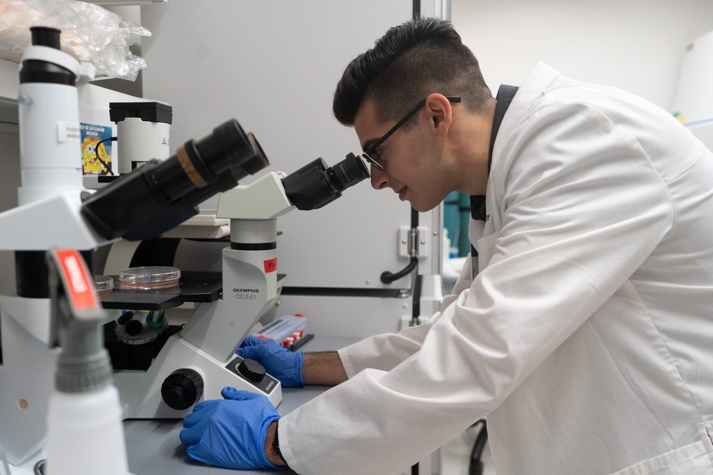 Ajay Tosh looking into a microscope while in a research laboratory.