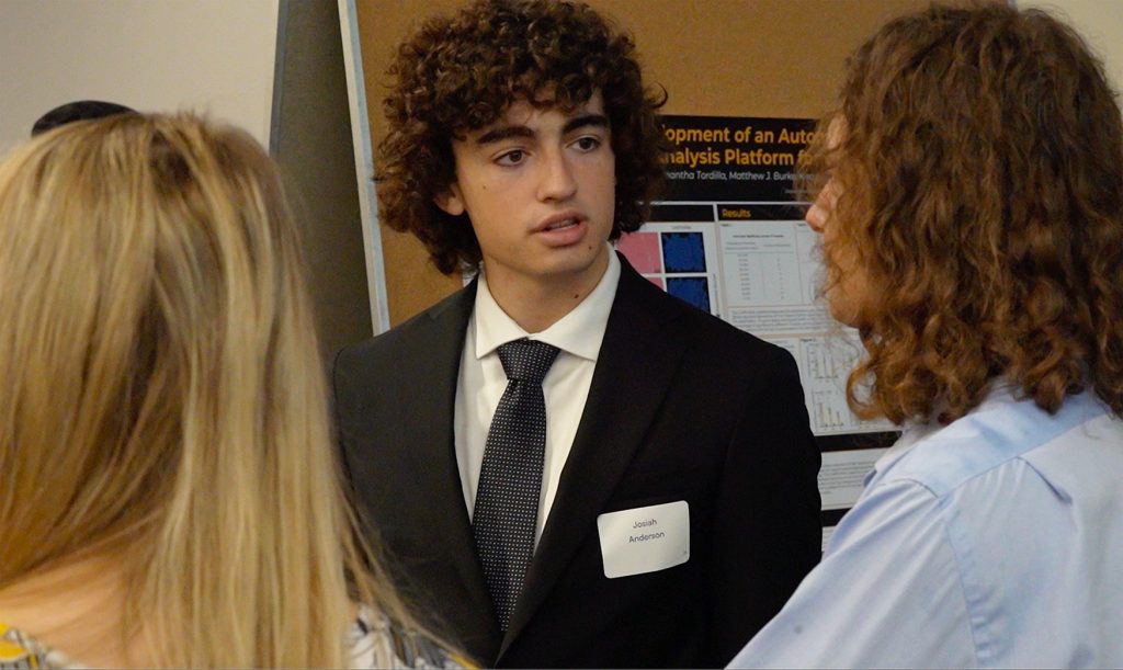 Josiah Anderson talking to an individual during a research presentation.